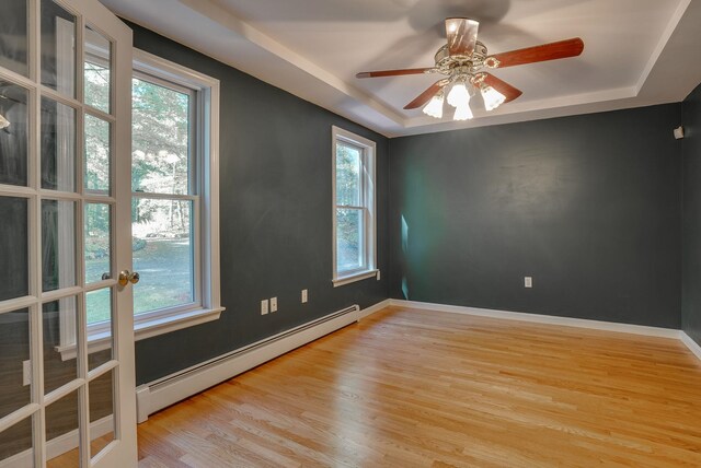 spare room featuring ceiling fan, baseboard heating, light wood-type flooring, and a tray ceiling