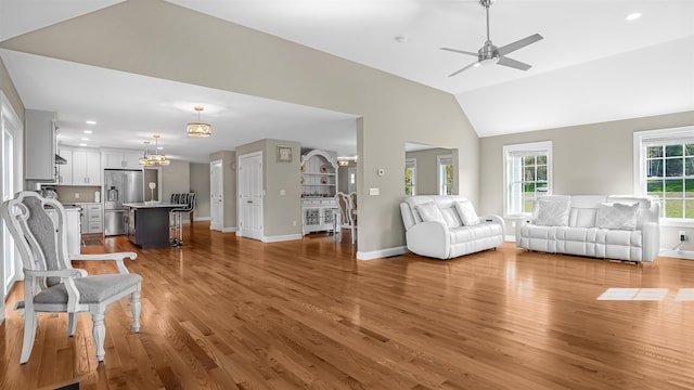 unfurnished living room with light wood-type flooring, ceiling fan with notable chandelier, and lofted ceiling