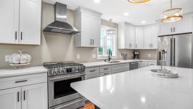 kitchen featuring hanging light fixtures, sink, wall chimney range hood, white cabinetry, and stainless steel appliances