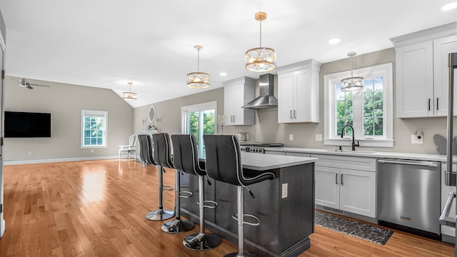 kitchen featuring appliances with stainless steel finishes, white cabinetry, light wood-type flooring, sink, and wall chimney range hood