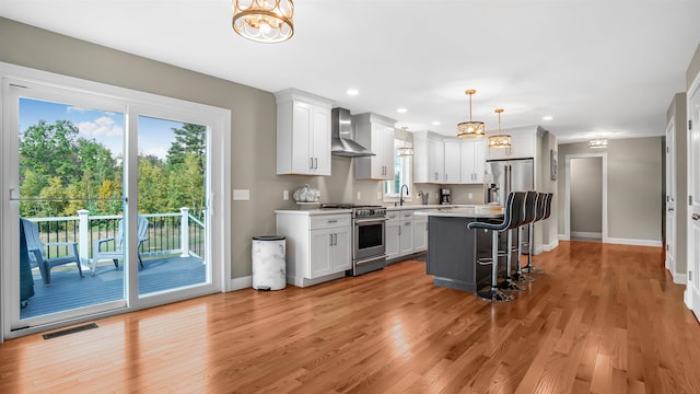 kitchen with appliances with stainless steel finishes, white cabinetry, a breakfast bar, wall chimney exhaust hood, and a kitchen island