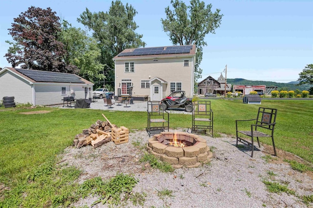 rear view of house featuring a lawn, solar panels, an outdoor fire pit, and a patio area