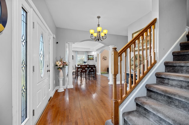 entrance foyer with a notable chandelier, decorative columns, and hardwood / wood-style flooring