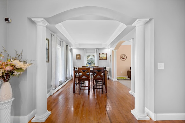 dining room featuring a tray ceiling, decorative columns, and hardwood / wood-style flooring