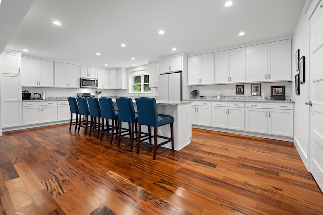 kitchen featuring a kitchen breakfast bar, white refrigerator, white cabinets, light stone countertops, and hardwood / wood-style flooring