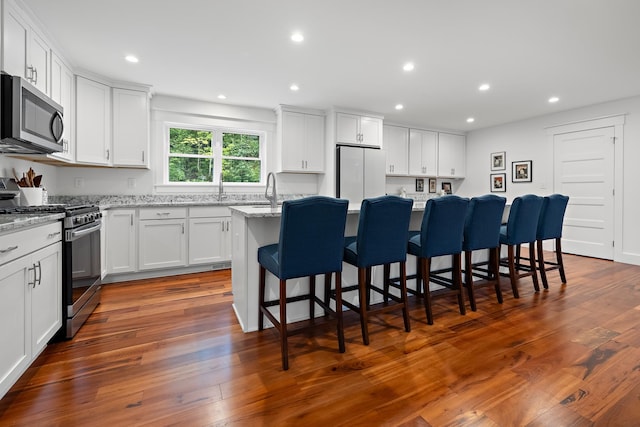 kitchen with appliances with stainless steel finishes, white cabinetry, dark hardwood / wood-style floors, and a breakfast bar