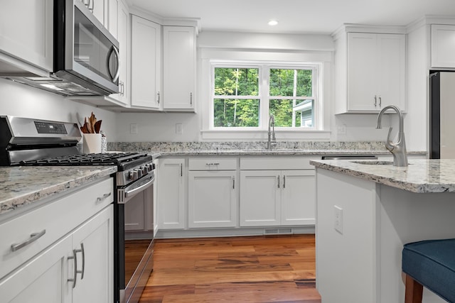 kitchen featuring appliances with stainless steel finishes, light stone counters, white cabinets, light hardwood / wood-style flooring, and sink