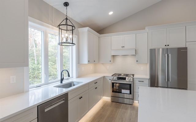 kitchen featuring sink, white cabinetry, stainless steel appliances, decorative light fixtures, and vaulted ceiling