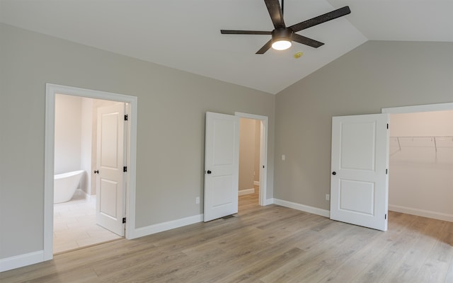 unfurnished bedroom featuring vaulted ceiling, ensuite bathroom, a walk in closet, light wood-type flooring, and a closet