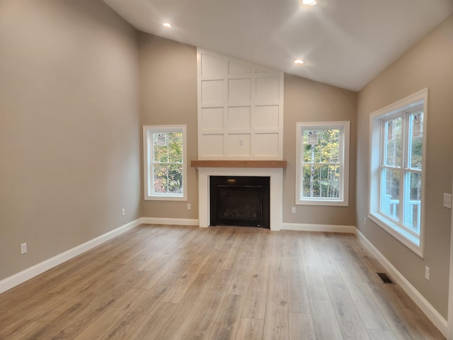 unfurnished living room with lofted ceiling, a large fireplace, and light hardwood / wood-style flooring