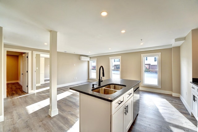 kitchen with white cabinets, dishwasher, a wall mounted AC, an island with sink, and sink