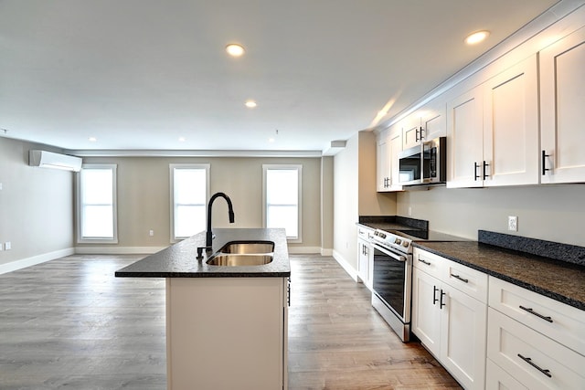 kitchen with a kitchen island with sink, appliances with stainless steel finishes, a wall mounted AC, sink, and white cabinetry