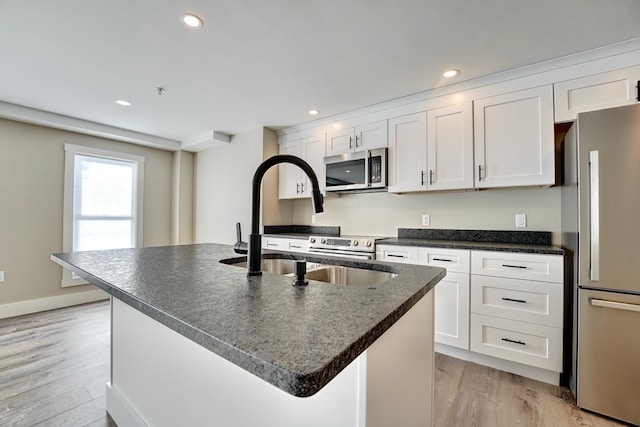 kitchen featuring white cabinets, a center island with sink, appliances with stainless steel finishes, and light hardwood / wood-style floors