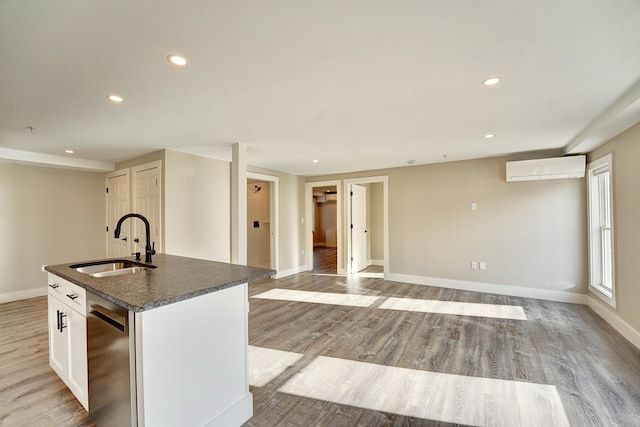 kitchen with a kitchen island with sink, a wall unit AC, sink, white cabinetry, and stainless steel dishwasher