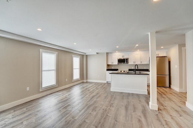 kitchen with a kitchen island with sink, appliances with stainless steel finishes, light wood-type flooring, sink, and white cabinetry