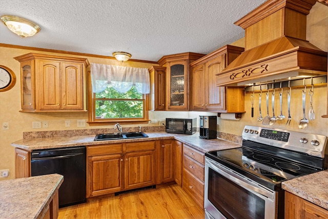 kitchen with custom exhaust hood, sink, a textured ceiling, black appliances, and light hardwood / wood-style floors