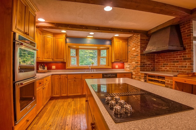 kitchen with wall chimney exhaust hood, stainless steel appliances, light hardwood / wood-style floors, and beamed ceiling