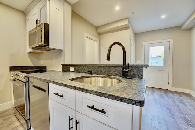 kitchen with light hardwood / wood-style floors, white cabinets, appliances with stainless steel finishes, dark stone countertops, and sink