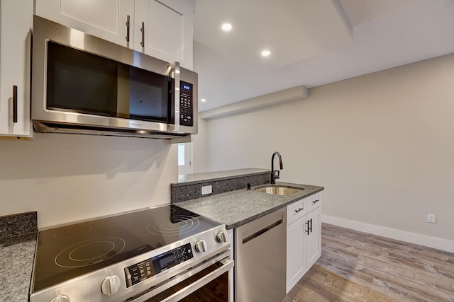 kitchen featuring stainless steel appliances, light wood-type flooring, stone counters, sink, and white cabinetry