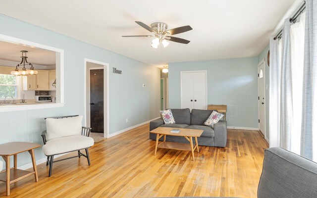 living room with ceiling fan with notable chandelier and light hardwood / wood-style floors