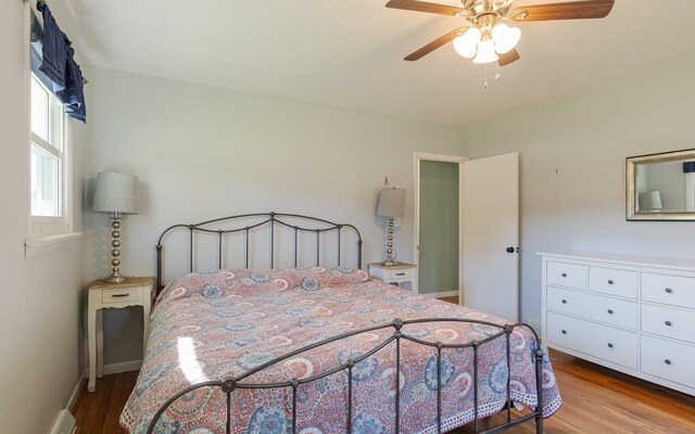 bedroom with ceiling fan, light wood-type flooring, and a baseboard heating unit