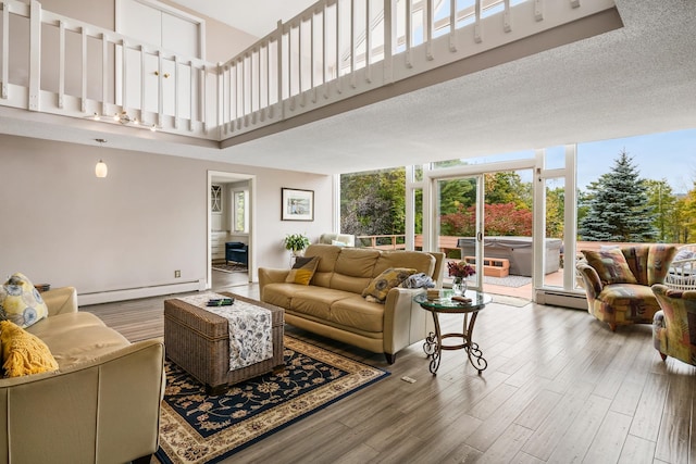 living room featuring a textured ceiling, hardwood / wood-style floors, baseboard heating, and plenty of natural light