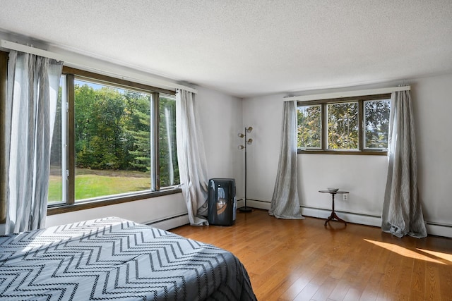 bedroom with a textured ceiling, light hardwood / wood-style floors, and a baseboard heating unit