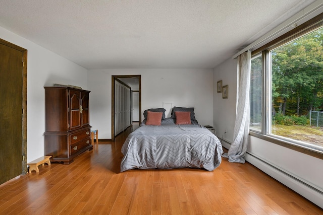 bedroom featuring multiple windows, a textured ceiling, a baseboard heating unit, and light hardwood / wood-style flooring