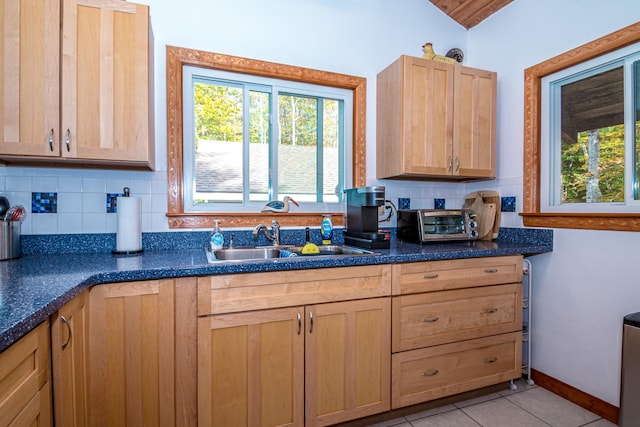 kitchen featuring a healthy amount of sunlight, light tile patterned flooring, vaulted ceiling, and sink