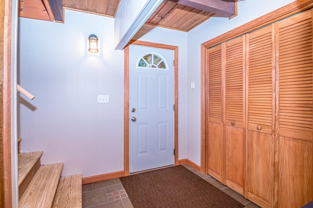 entryway with wooden walls, wood ceiling, beam ceiling, and dark tile patterned floors