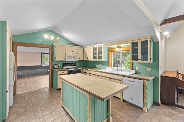 kitchen with white appliances, a center island, cream cabinets, vaulted ceiling, and light countertops