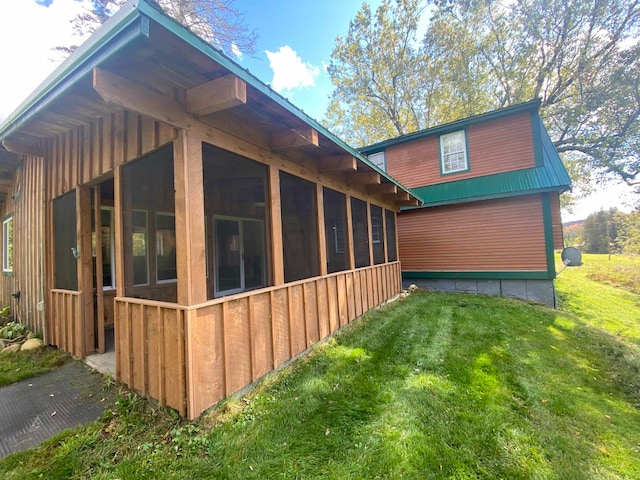 view of side of home featuring a lawn, metal roof, board and batten siding, and a sunroom
