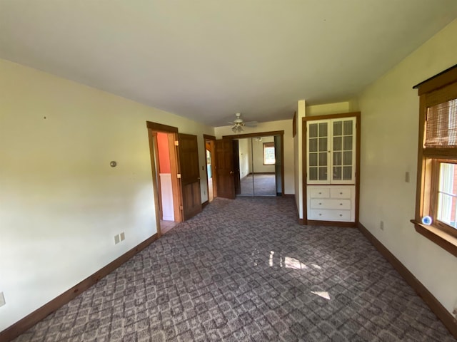 empty room with ceiling fan, dark colored carpet, and baseboards
