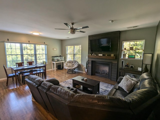 living room with ceiling fan, hardwood / wood-style flooring, and a large fireplace