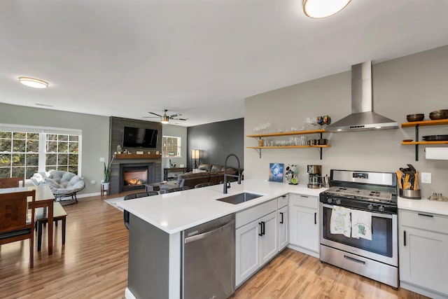 kitchen with sink, kitchen peninsula, wall chimney exhaust hood, light hardwood / wood-style flooring, and appliances with stainless steel finishes