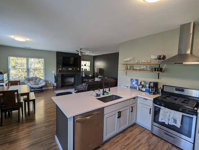 kitchen featuring dark hardwood / wood-style floors, kitchen peninsula, wall chimney range hood, stainless steel appliances, and a large fireplace