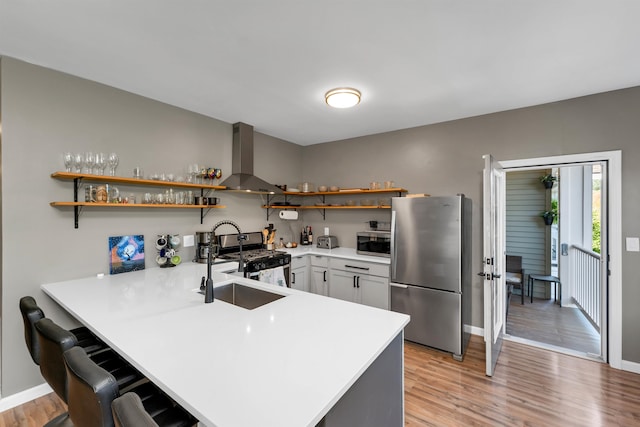 kitchen featuring appliances with stainless steel finishes, light hardwood / wood-style floors, kitchen peninsula, a breakfast bar area, and wall chimney range hood