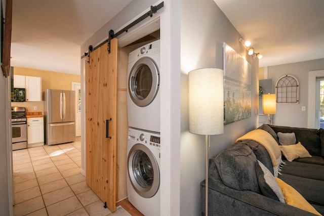 clothes washing area featuring light tile patterned flooring, a barn door, and stacked washer and dryer