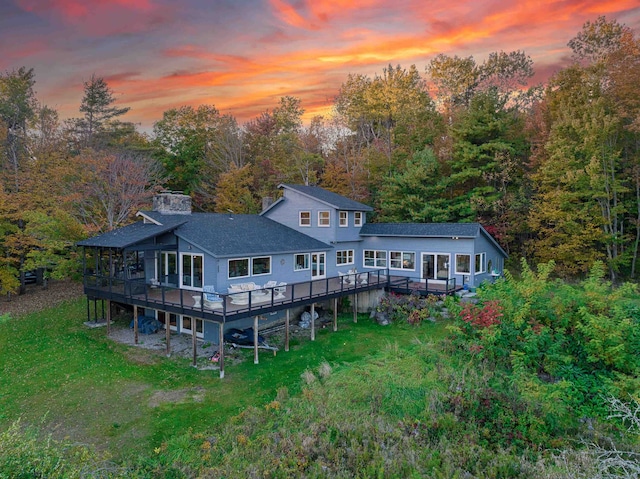 back house at dusk with a lawn and a wooden deck