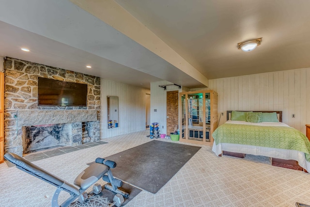 bedroom with carpet flooring, a stone fireplace, and wooden walls