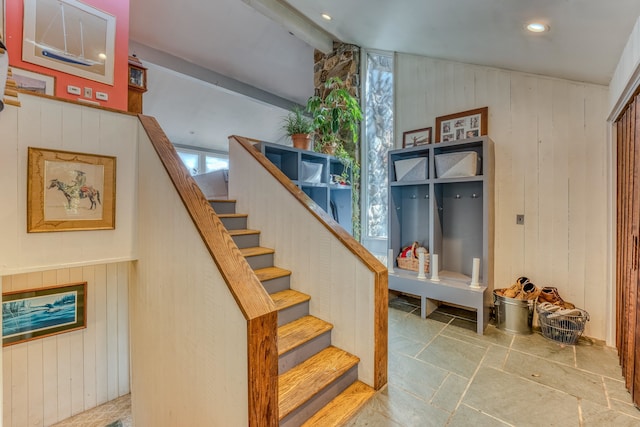 stairway featuring beam ceiling and wooden walls