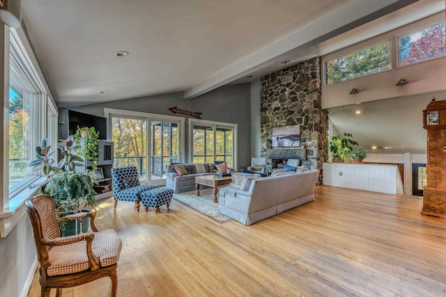 living room with vaulted ceiling with beams, light hardwood / wood-style floors, and a stone fireplace