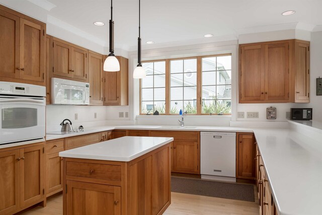 kitchen with sink, light wood-type flooring, hanging light fixtures, a center island, and white appliances