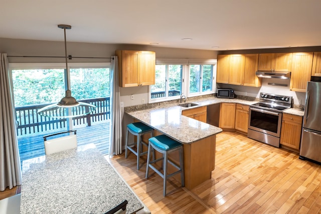 kitchen with light wood-type flooring, sink, a kitchen breakfast bar, appliances with stainless steel finishes, and decorative light fixtures