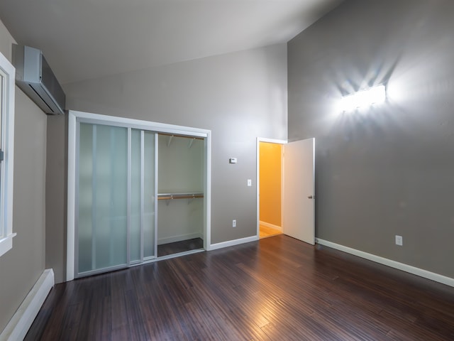 unfurnished bedroom with dark wood-type flooring, high vaulted ceiling, a closet, a baseboard heating unit, and a wall mounted air conditioner