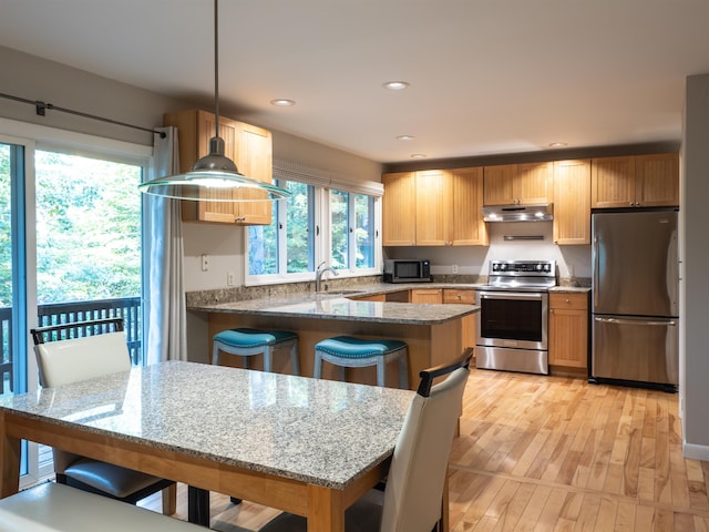 kitchen featuring dark stone counters, light hardwood / wood-style floors, a kitchen bar, stainless steel appliances, and decorative light fixtures