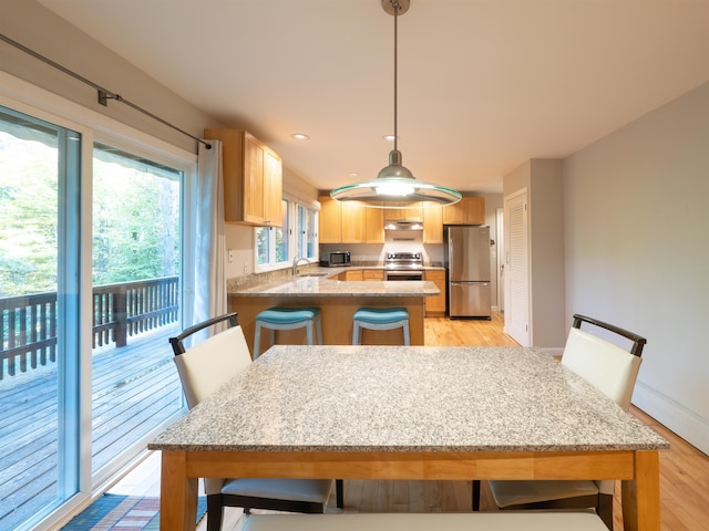 kitchen with appliances with stainless steel finishes, kitchen peninsula, a breakfast bar area, light wood-type flooring, and decorative light fixtures