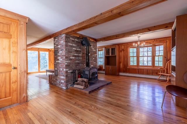 unfurnished living room featuring baseboard heating, a wood stove, a healthy amount of sunlight, and light wood-type flooring