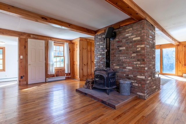 unfurnished living room with beam ceiling, a wood stove, a baseboard heating unit, and light wood-type flooring