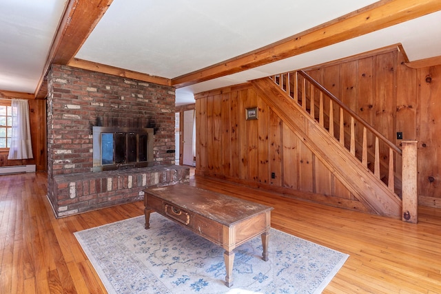 living room featuring beam ceiling, a brick fireplace, wooden walls, and light wood-type flooring